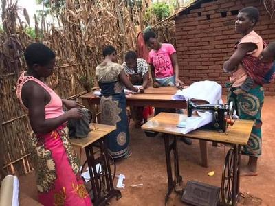 Widows being taught the trade of sewing on a machine